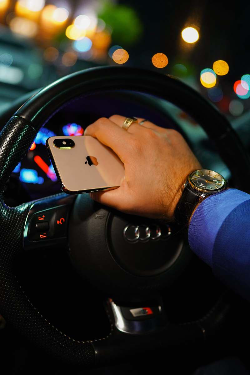 electronics person holding gold iPhone Xs while driving black Audi vehicle phone